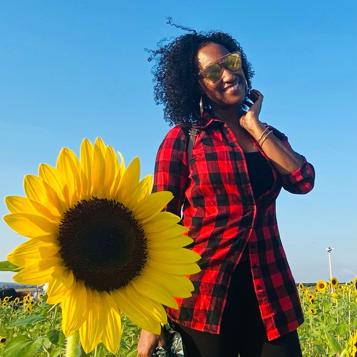 Lauren Pitcairn smiles while posting with a sunflower in the foreground.