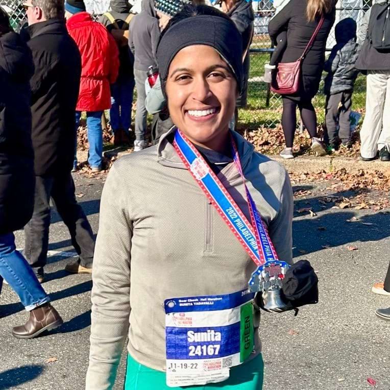 Sunita smiles and holds a medal after completing a race.