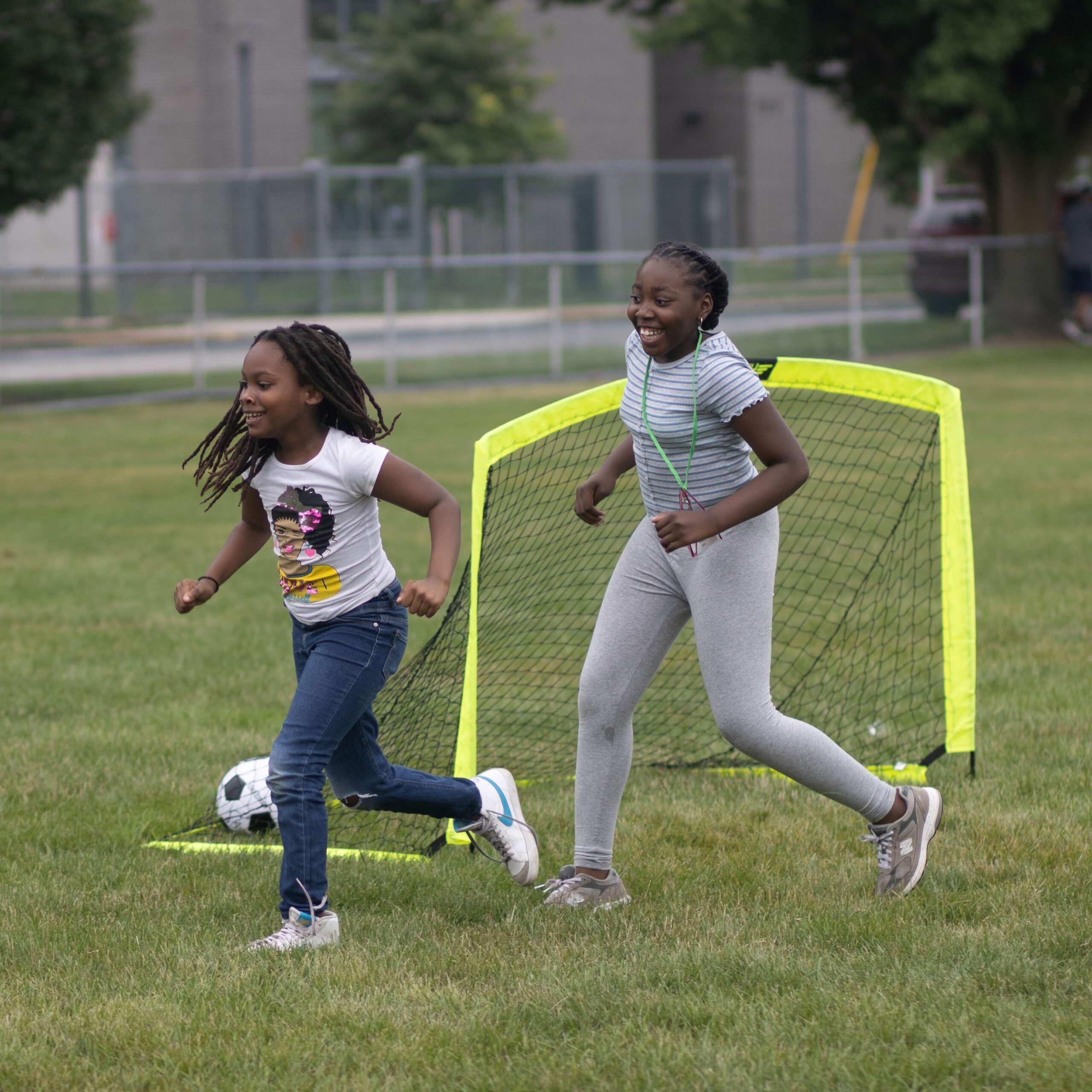 two girls run across a field playing soccer
