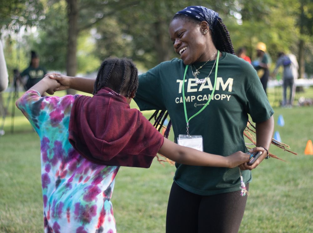 a camp counselor dances with a camper outside.