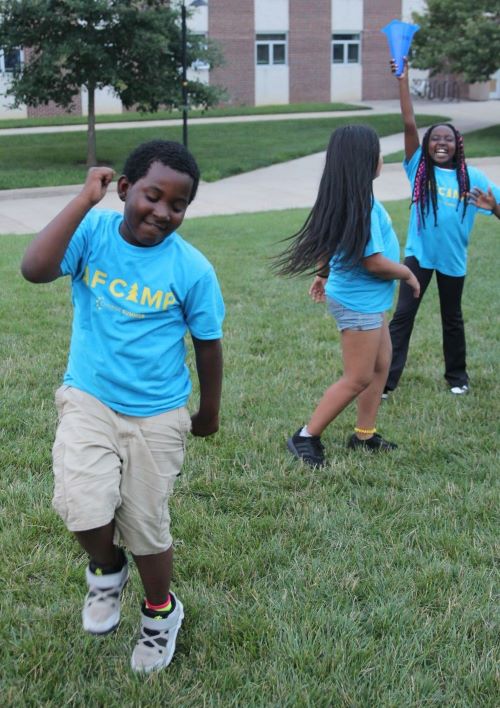 young boy dances outside while two girls dance near him.