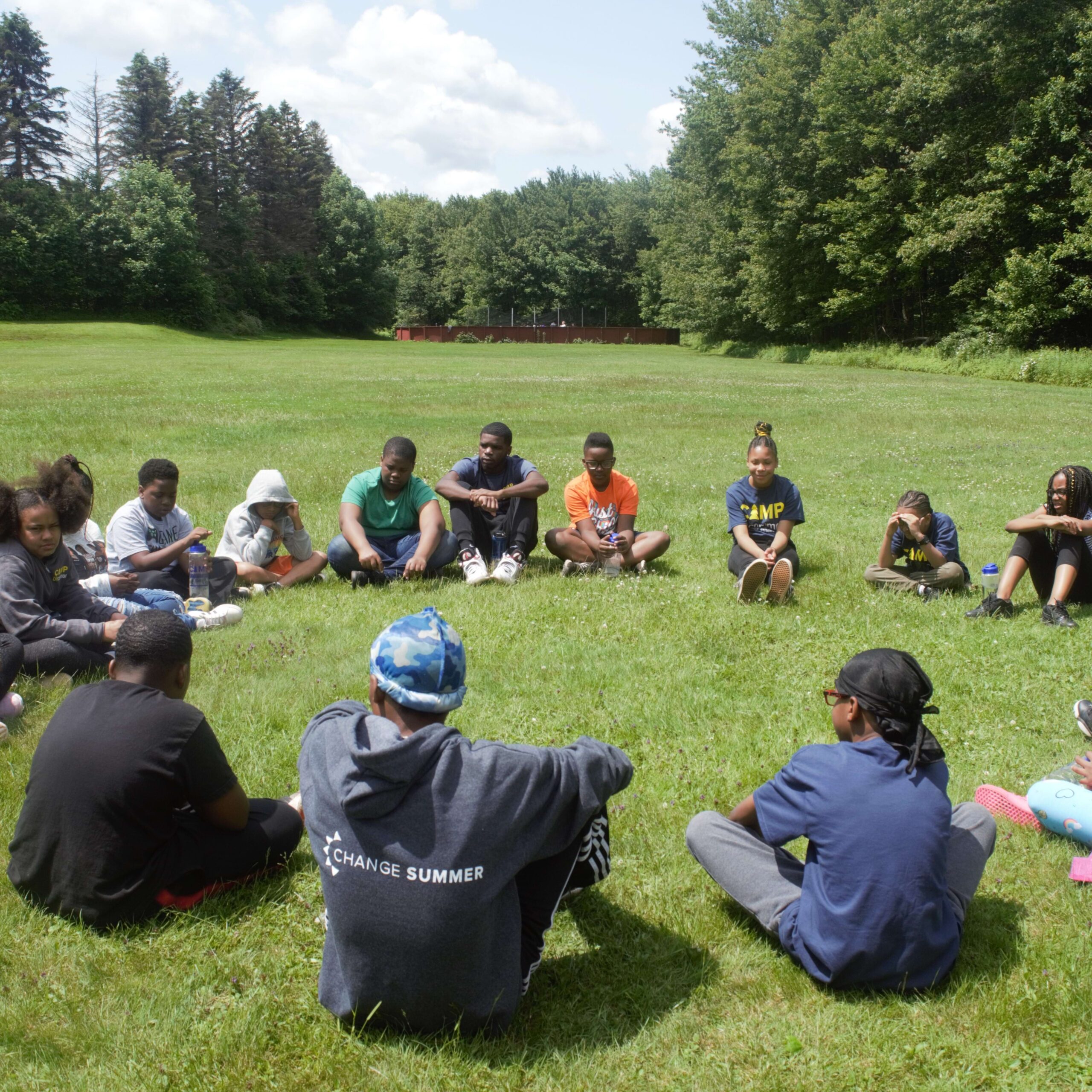 kids sitting in a circle in an open field surrounded by trees